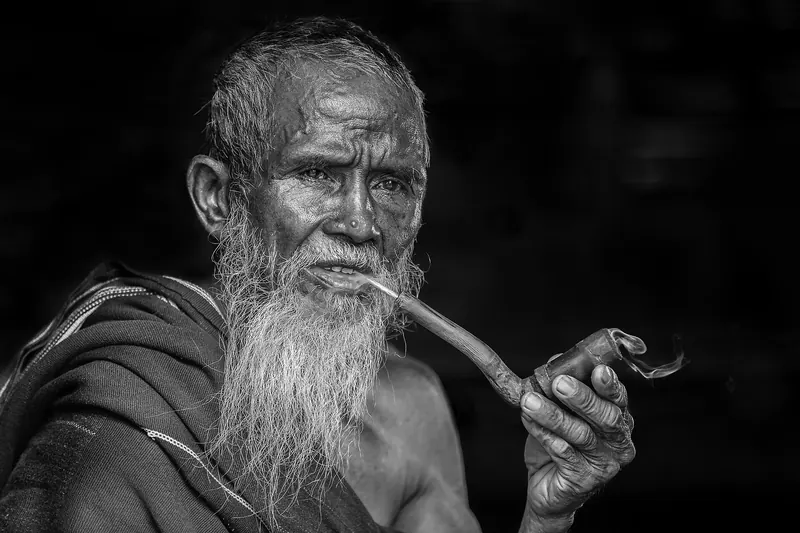 Portret alb-negru al unui bărbat cu barbă lungă, care fumează pipa
