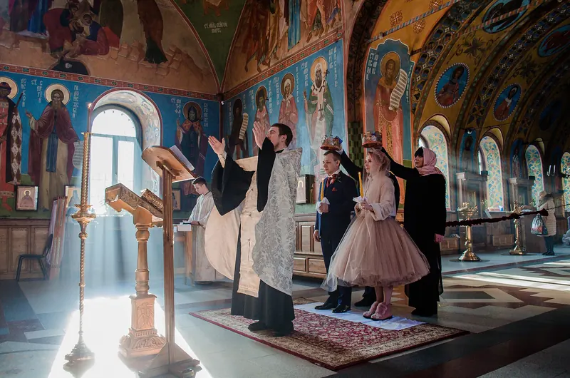 Ceremonie religioasă într-o biserică pictată, cu lumină ce intră pe ferestre
