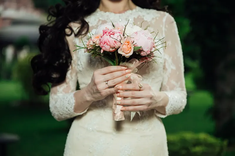 Mireasă ținând un buchet de trandafiri roz, în mâneci de dantelă